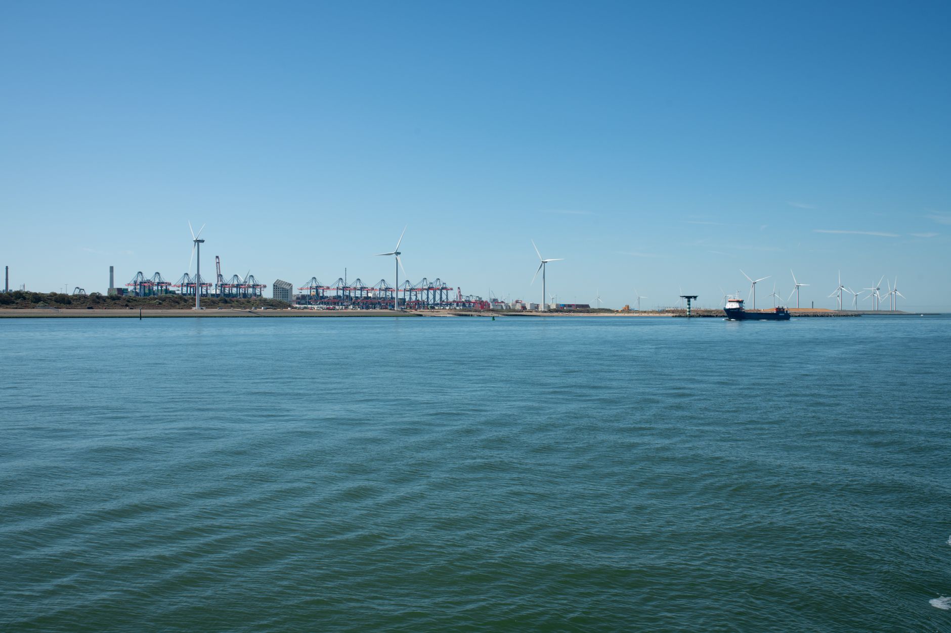 A scenic view of a coastal wind farm near a shipping port, showcasing renewable energy and maritime activity.