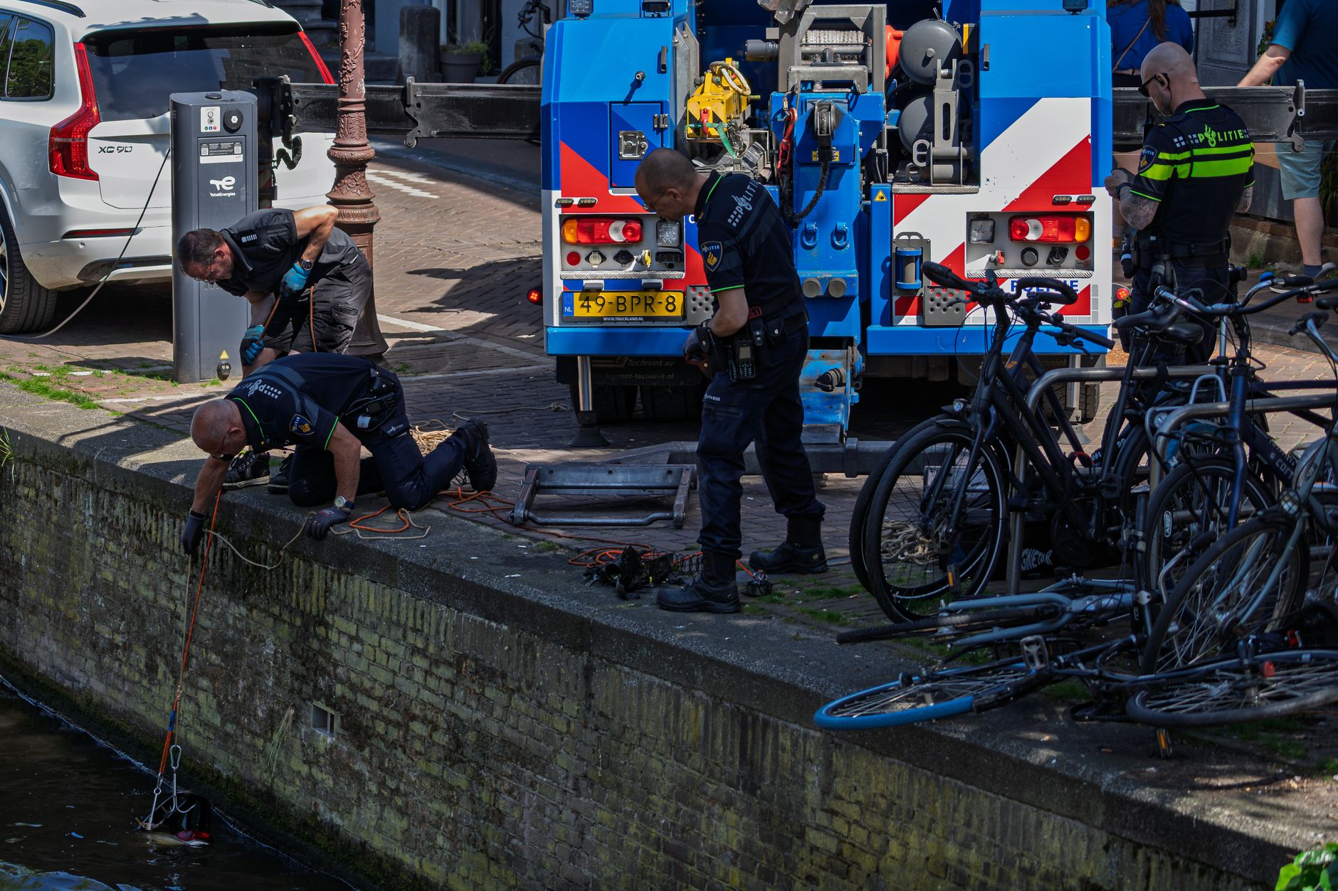 Police officers conducting a canal search operation in a city with bicycles nearby.