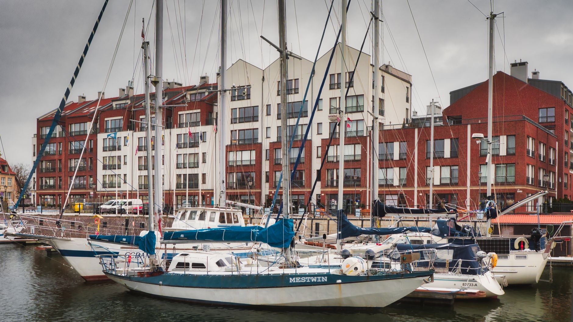 Scenic view of sailboats anchored in Gdańsk marina with modern buildings in the background.