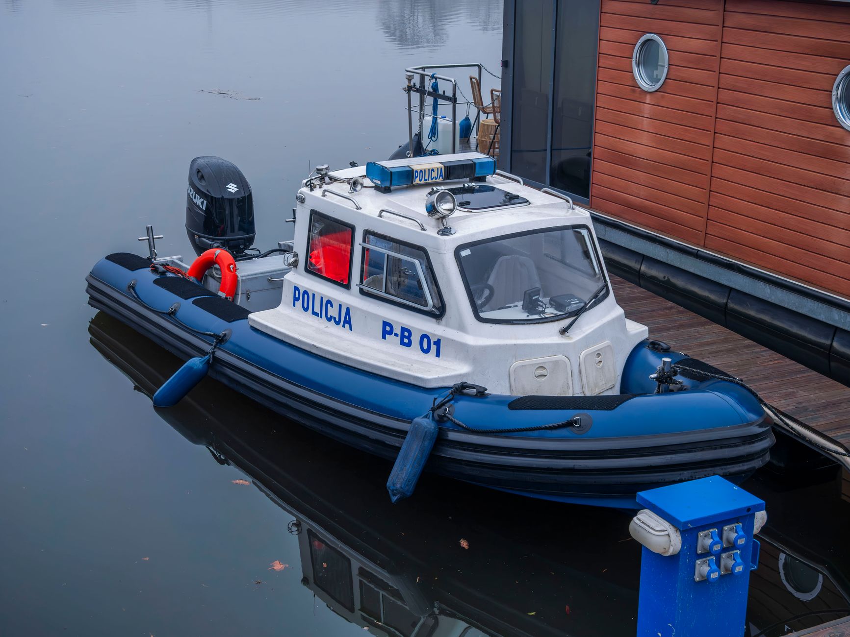 A police patrol boat docked beside a wooden structure on calm waters.
