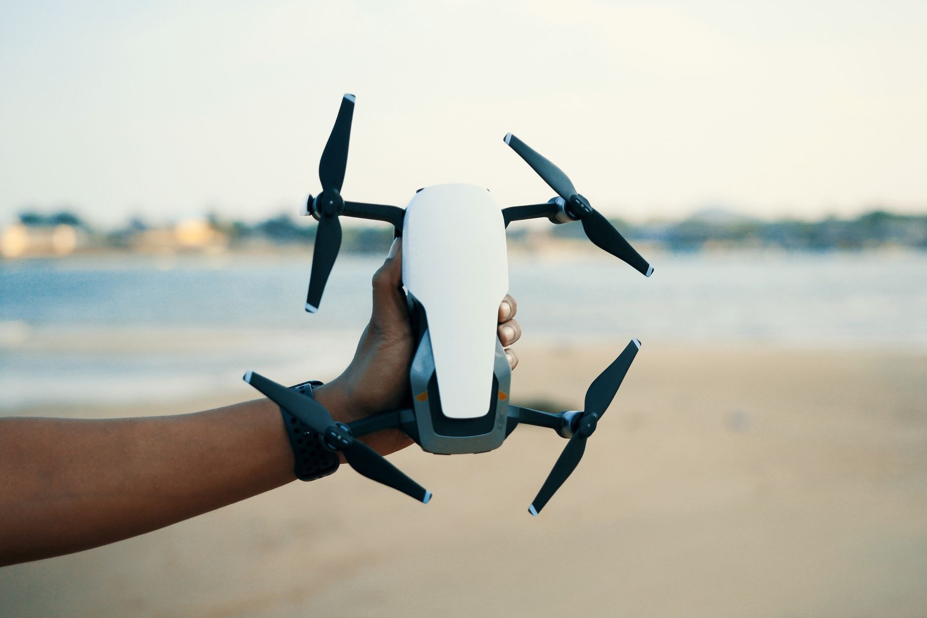 Close-up of a hand holding a drone on a beach during daytime, showcasing modern technology.