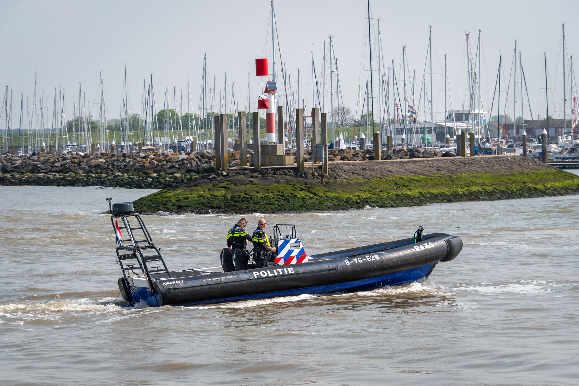 Police boat with officers patrolling near marina during the day.