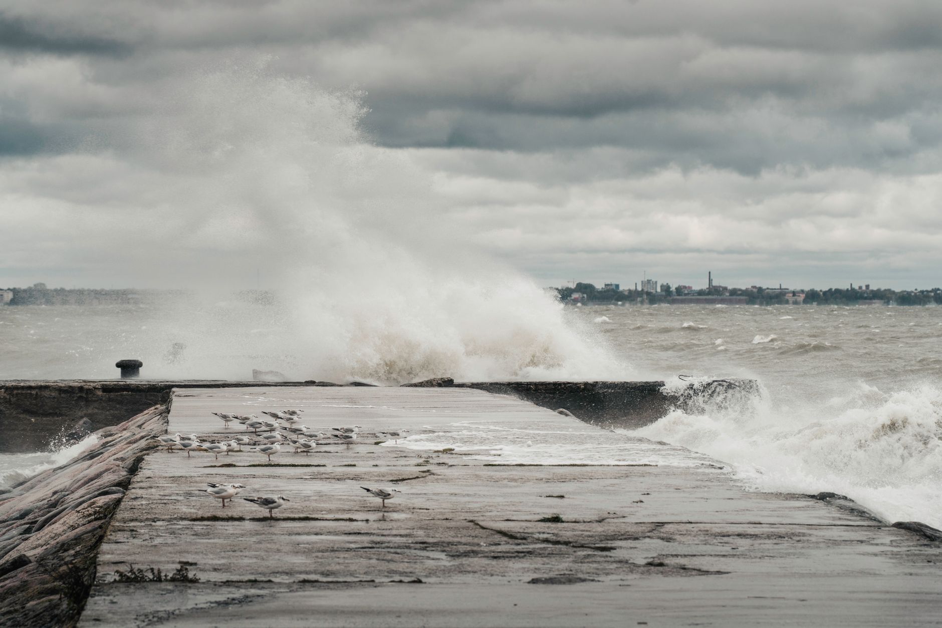 Stormy sea with waves crashing on a pier in Estonia, under a cloudy sky.