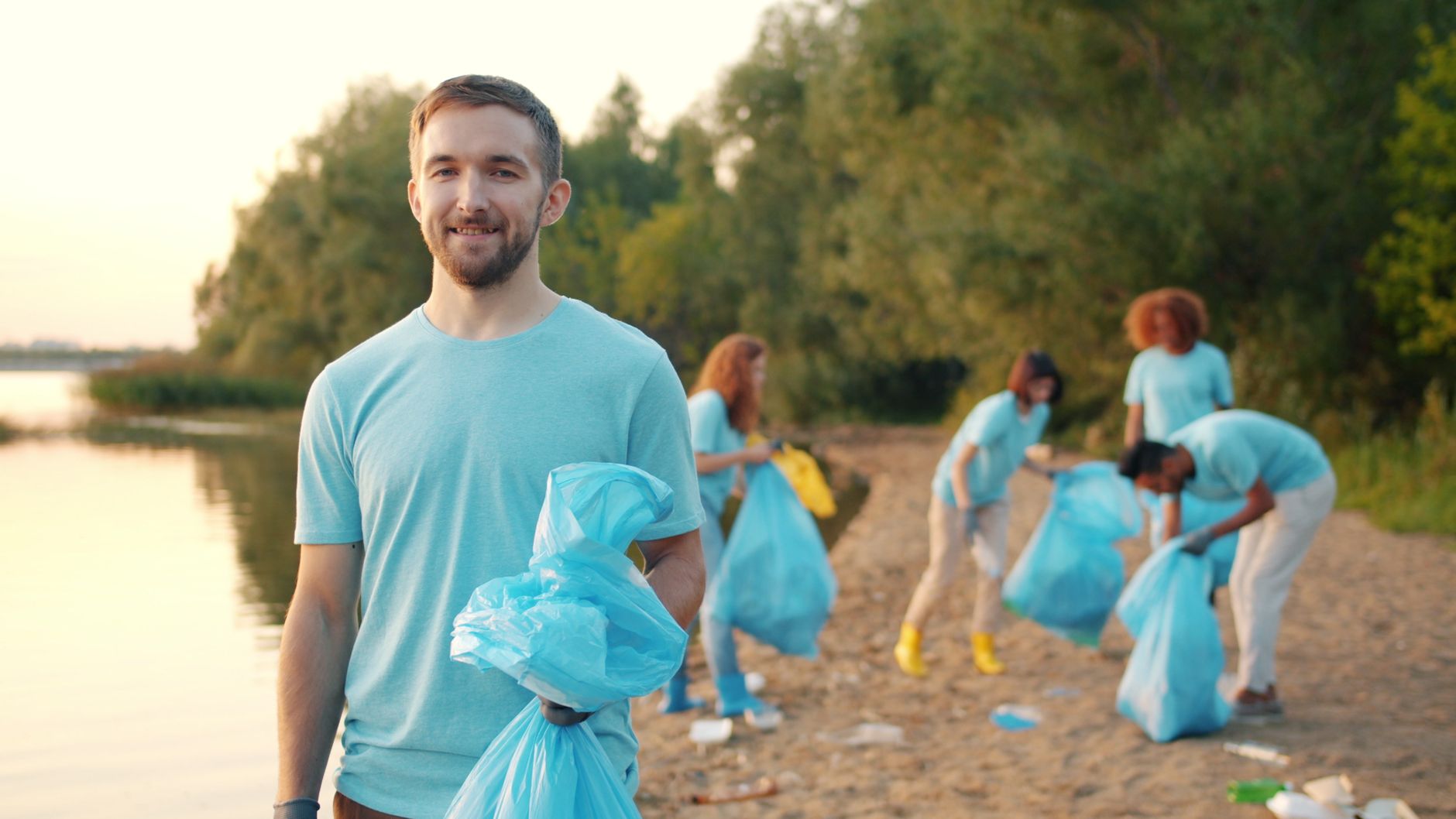 A group of volunteers cleaning a riverbank, collecting trash in blue bags. Outdoor community service.