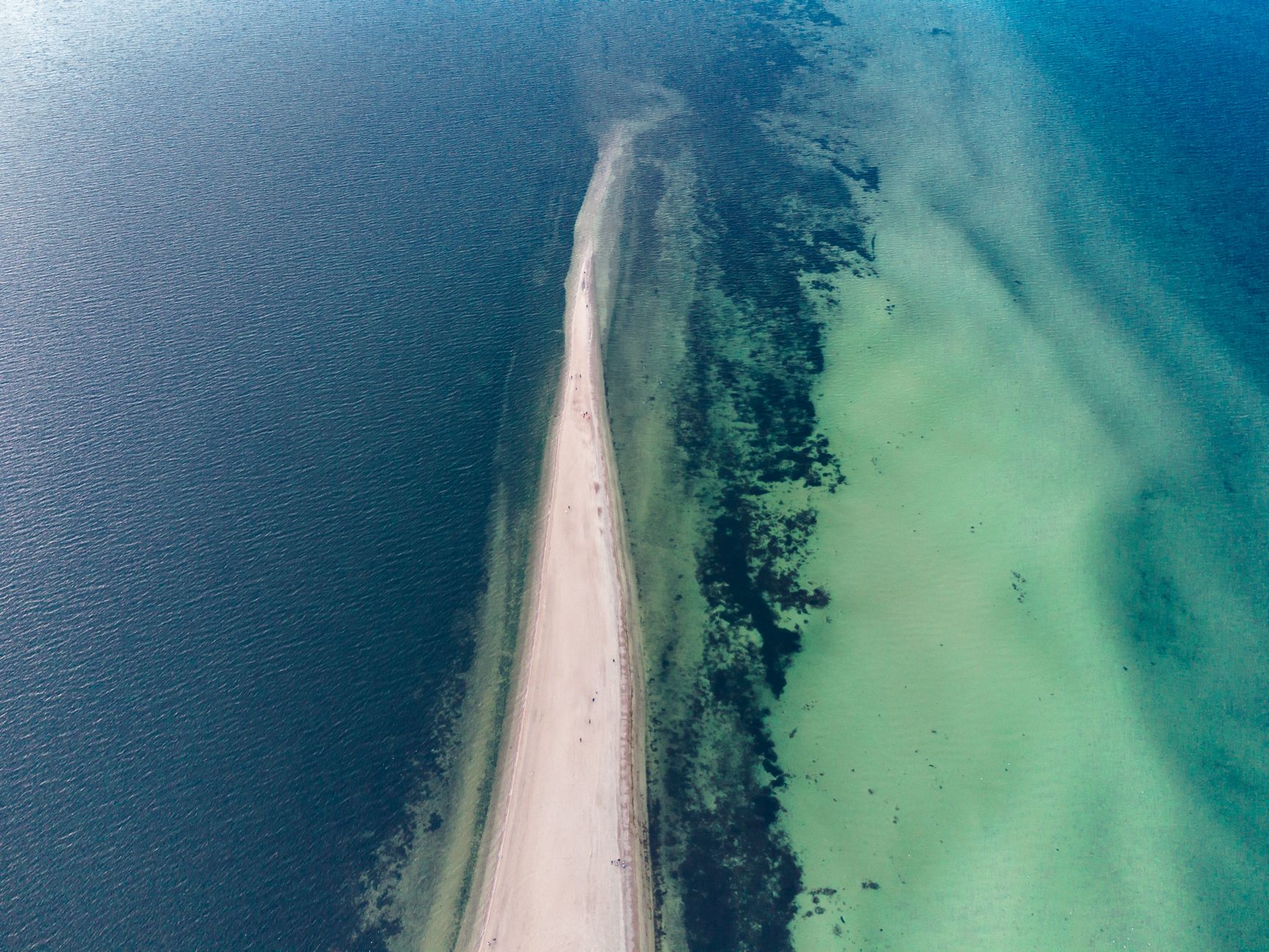 A scenic aerial view showcasing a sandy spit stretching into the blue-green waters of the Baltic Sea.