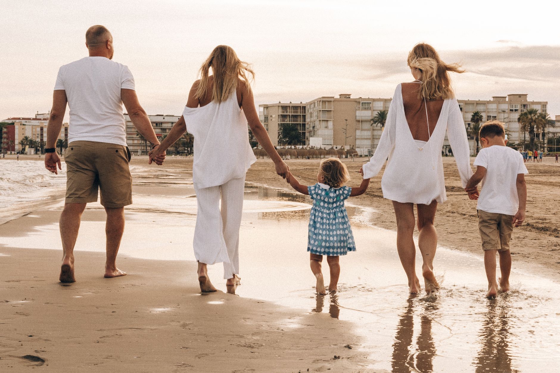 Family walking hand in hand along the beach at sunset, enjoying a warm summer day.