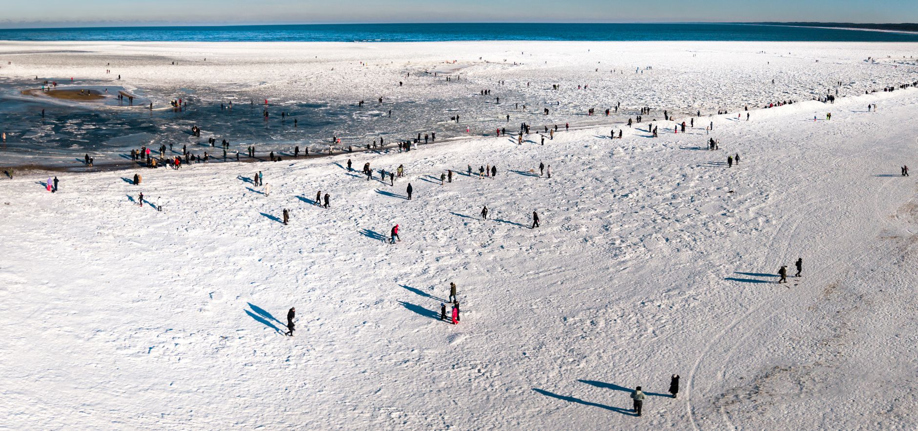 Aerial view of a snowy beach with scattered people enjoying the winter scenery.