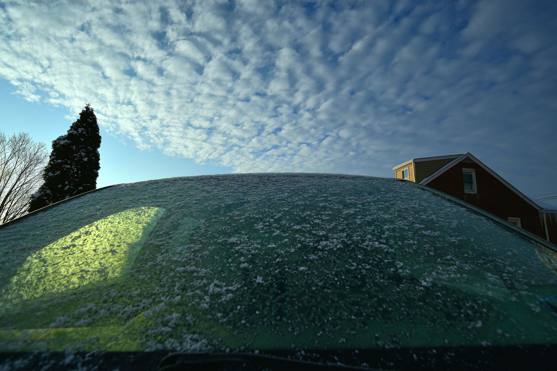 Frost covers a windshield in a suburban winter morning landscape.