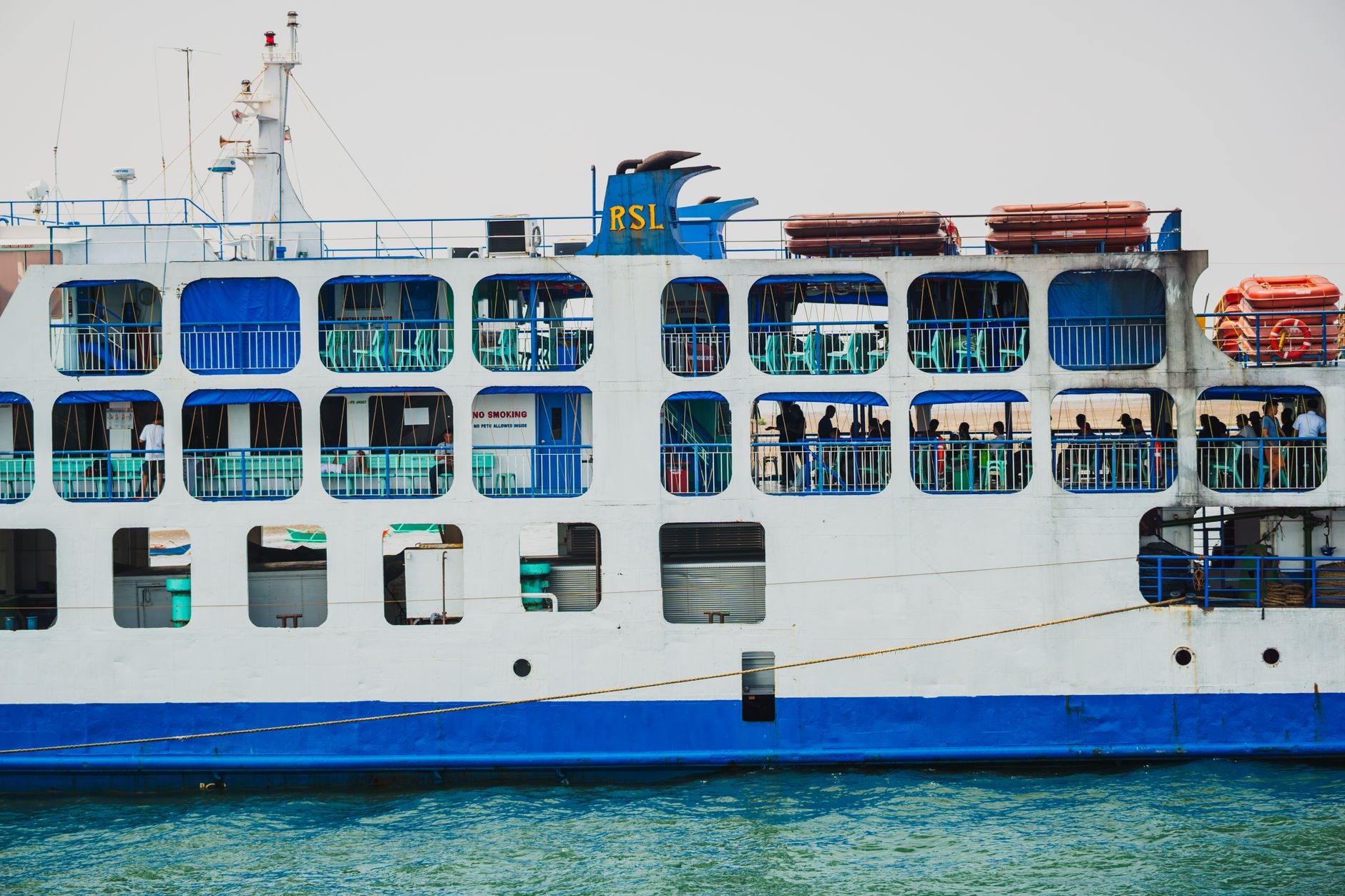 Side view of a passenger ferry with blue accents, showcasing people onboard and lifeboats.