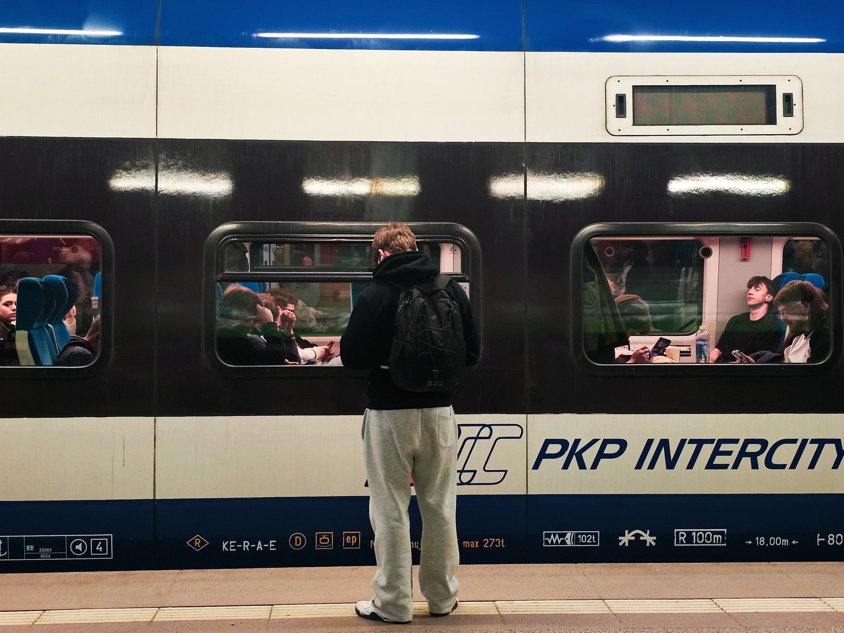 A busy PKP Intercity train scene at Wrocław station with passengers inside and traveler awaiting on the platform.